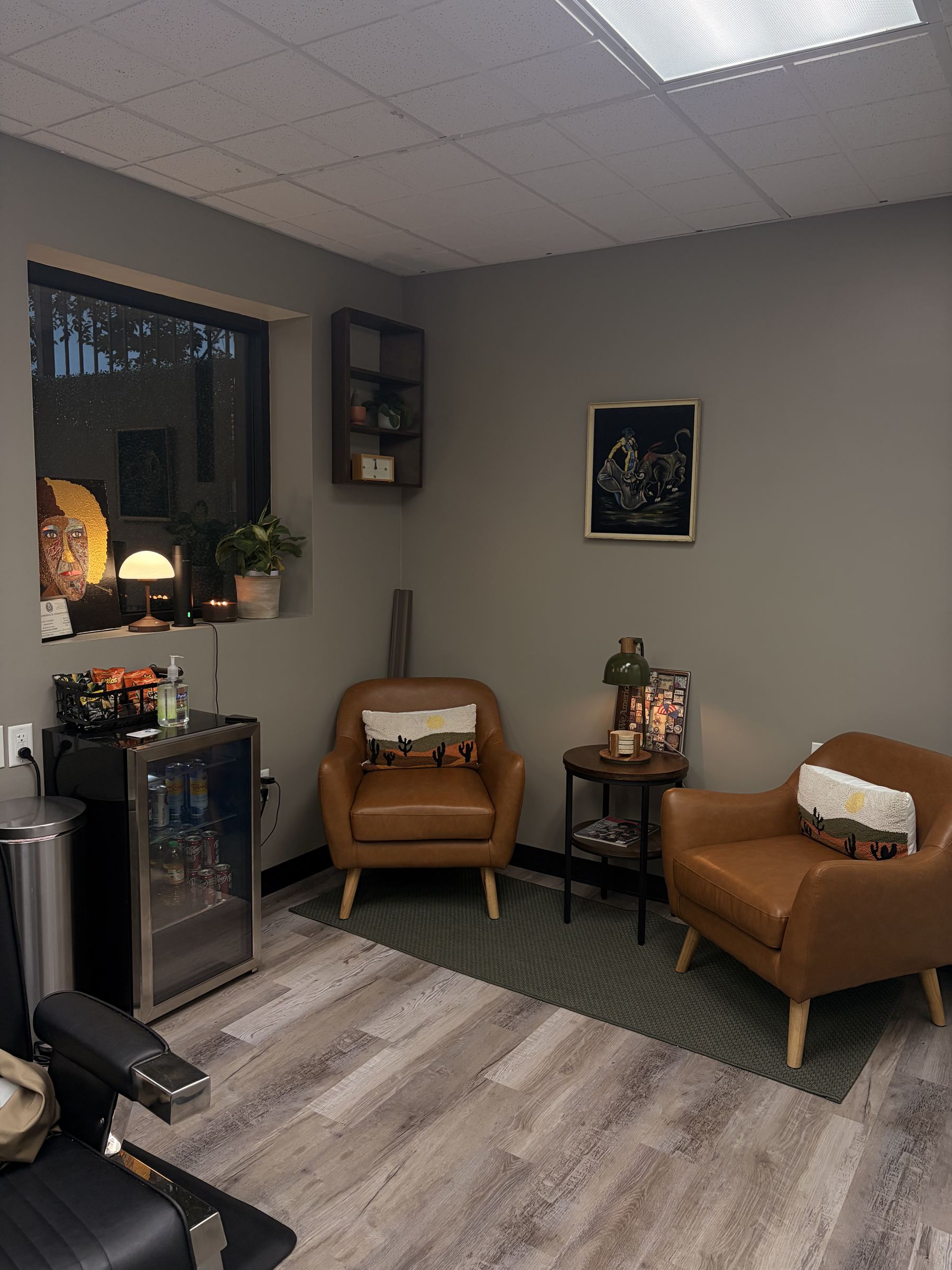 Leather lounge chairs and a stocked drink fridge in the Refined Barbers waiting area